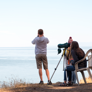 三个学生站在悬崖上俯瞰大海. 一个有双筒望远镜，另一个有瞄准镜.