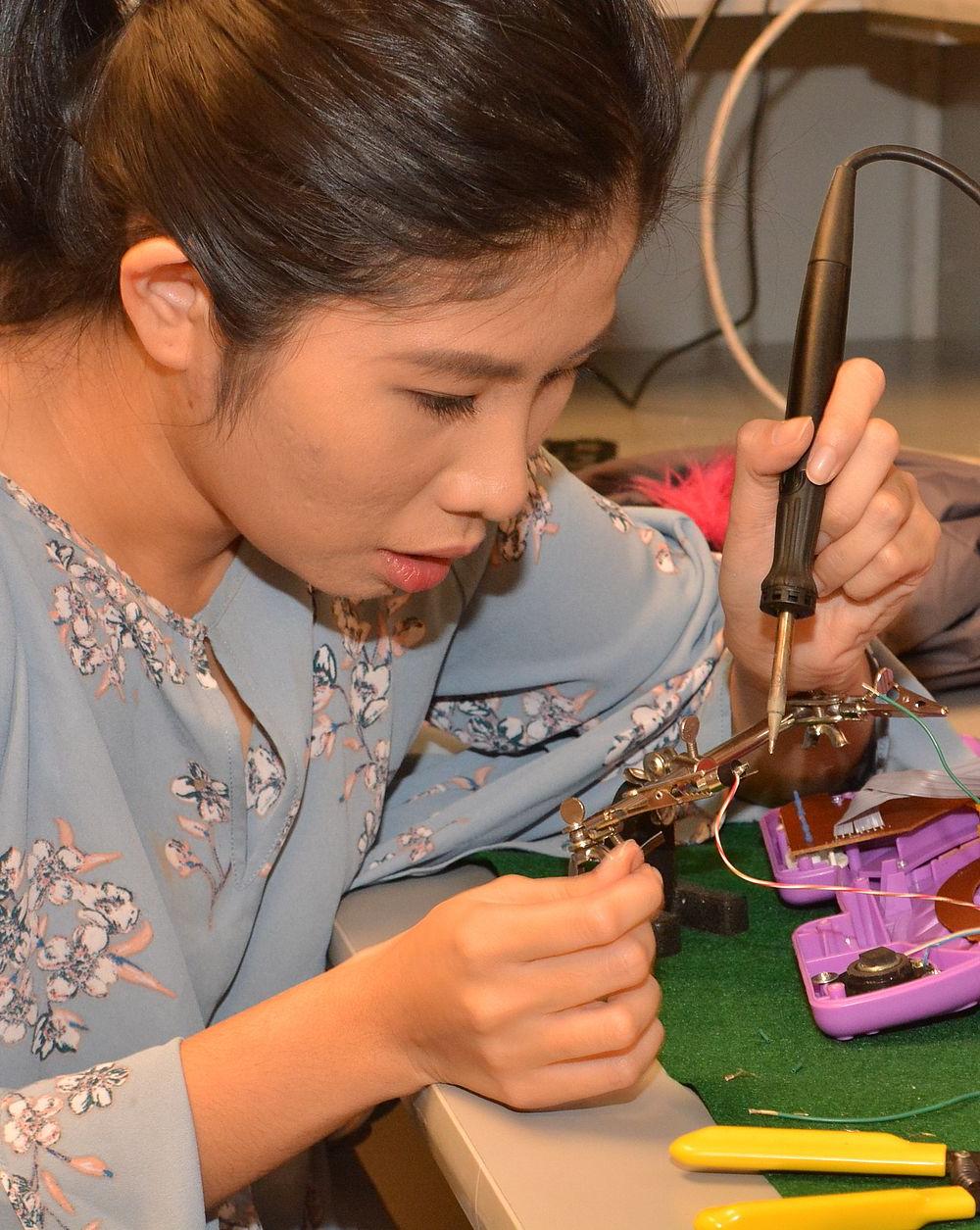 Female student solders wires on plastic toy. 